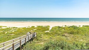 A beach with a wooden boardwalk leading to the shore, surrounded by green vegetation. - Superb Home With Private Walkover to Beach (Freeport)