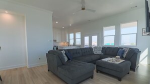 A spacious living room with a sectional sofa and ottoman, a kitchen in the background, and large windows providing natural light. - Unforgettable Vacation Getaway in Treasure Island (Freeport)