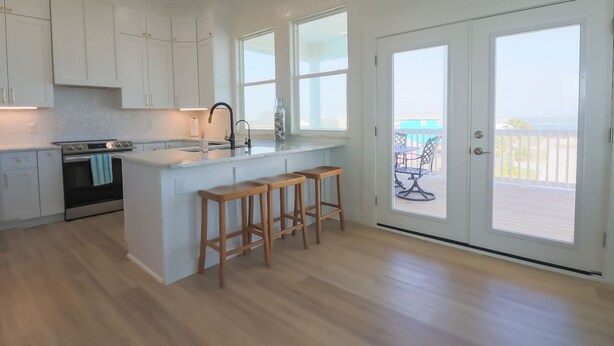 A modern kitchen with white cabinetry, a central island with stools, a built-in oven, and a large sliding glass door leading to a balcony with a view. - Unforgettable Vacation Getaway in Treasure Island (Freeport)