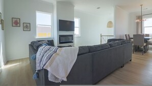 A modern living room with a grey sectional sofa, a flat-screen TV, and a dining area with a table and chairs. - Unforgettable Vacation Getaway in Treasure Island (Freeport)