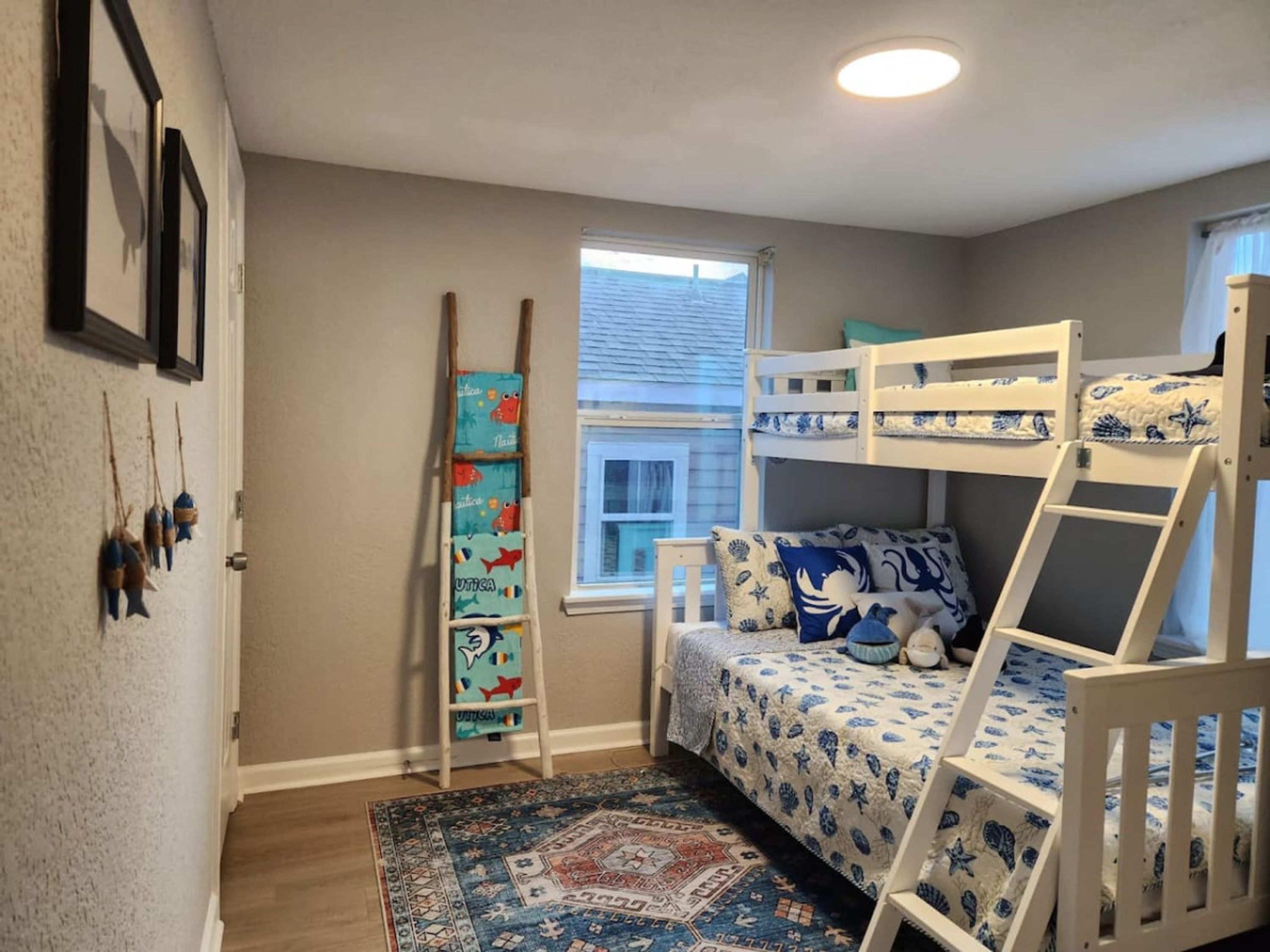 Een kinderkamer met stapelbedden, een ladder, een raam en een vloerkleed.
