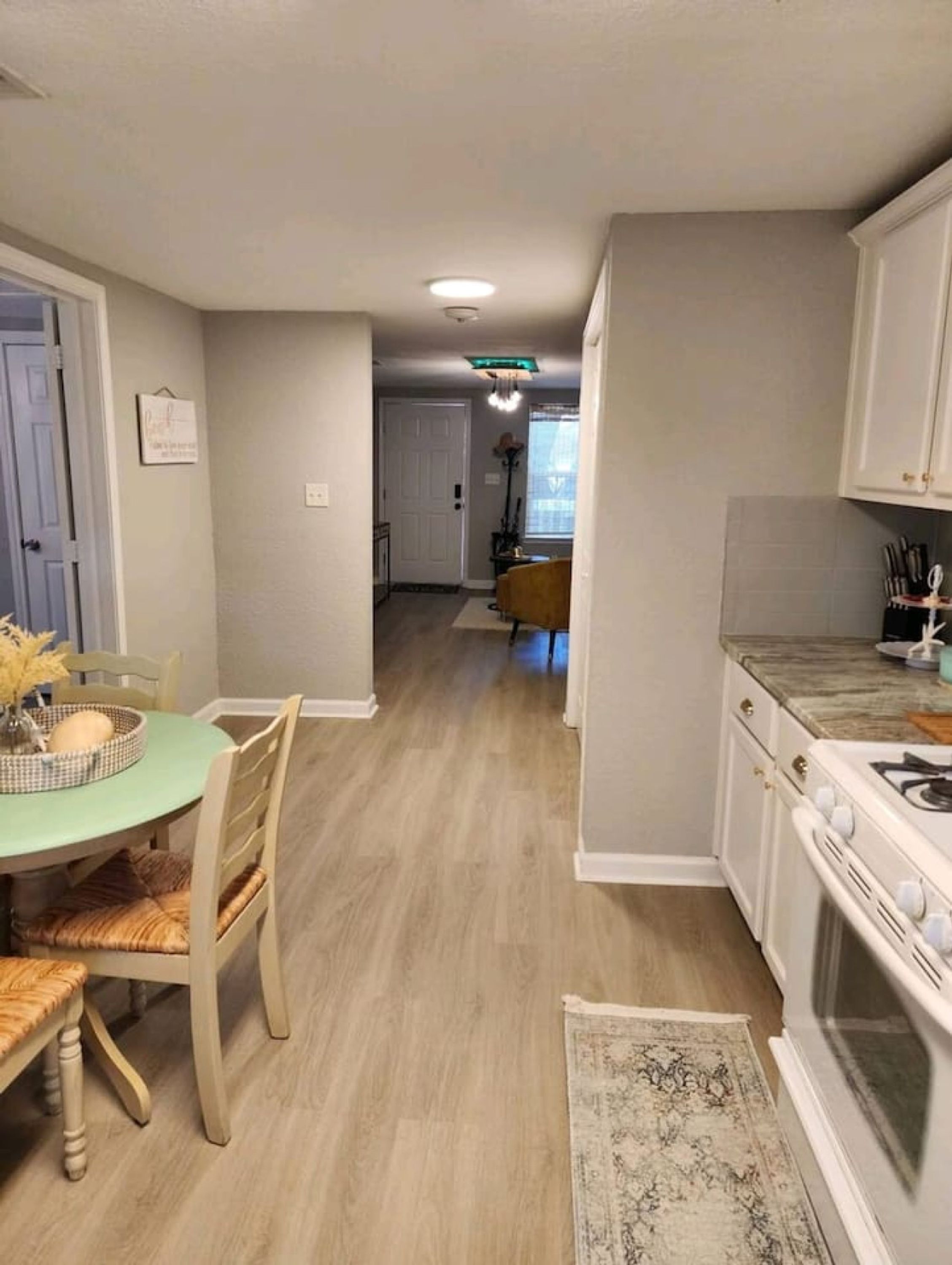 Una cocina con armarios blancos, una estufa y un comedor con mesa y sillas.