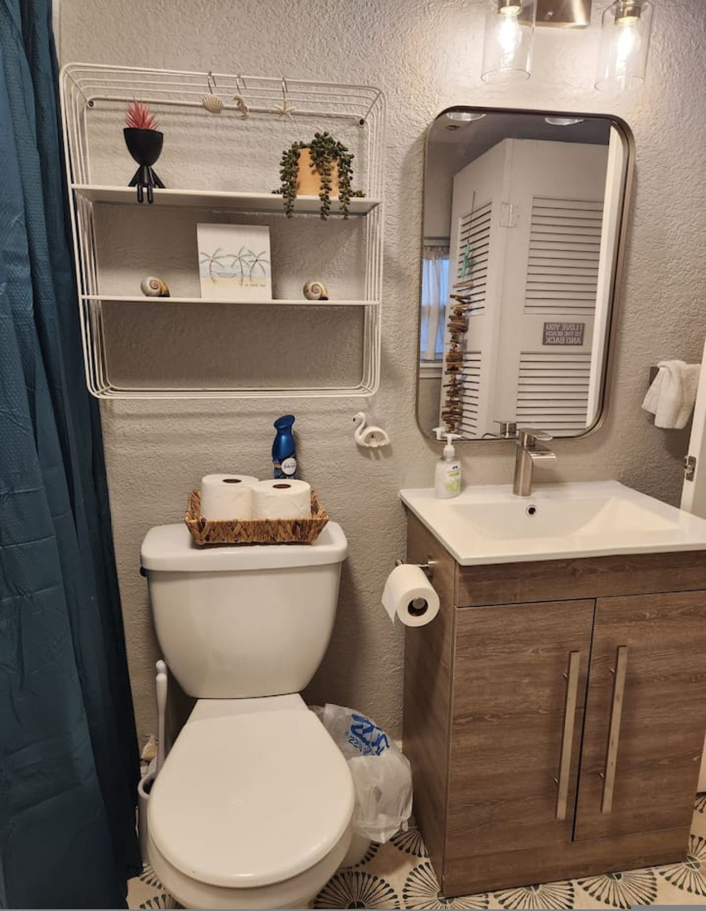 A bathroom with a toilet, a sink, a mirror, and shelves with toiletries.