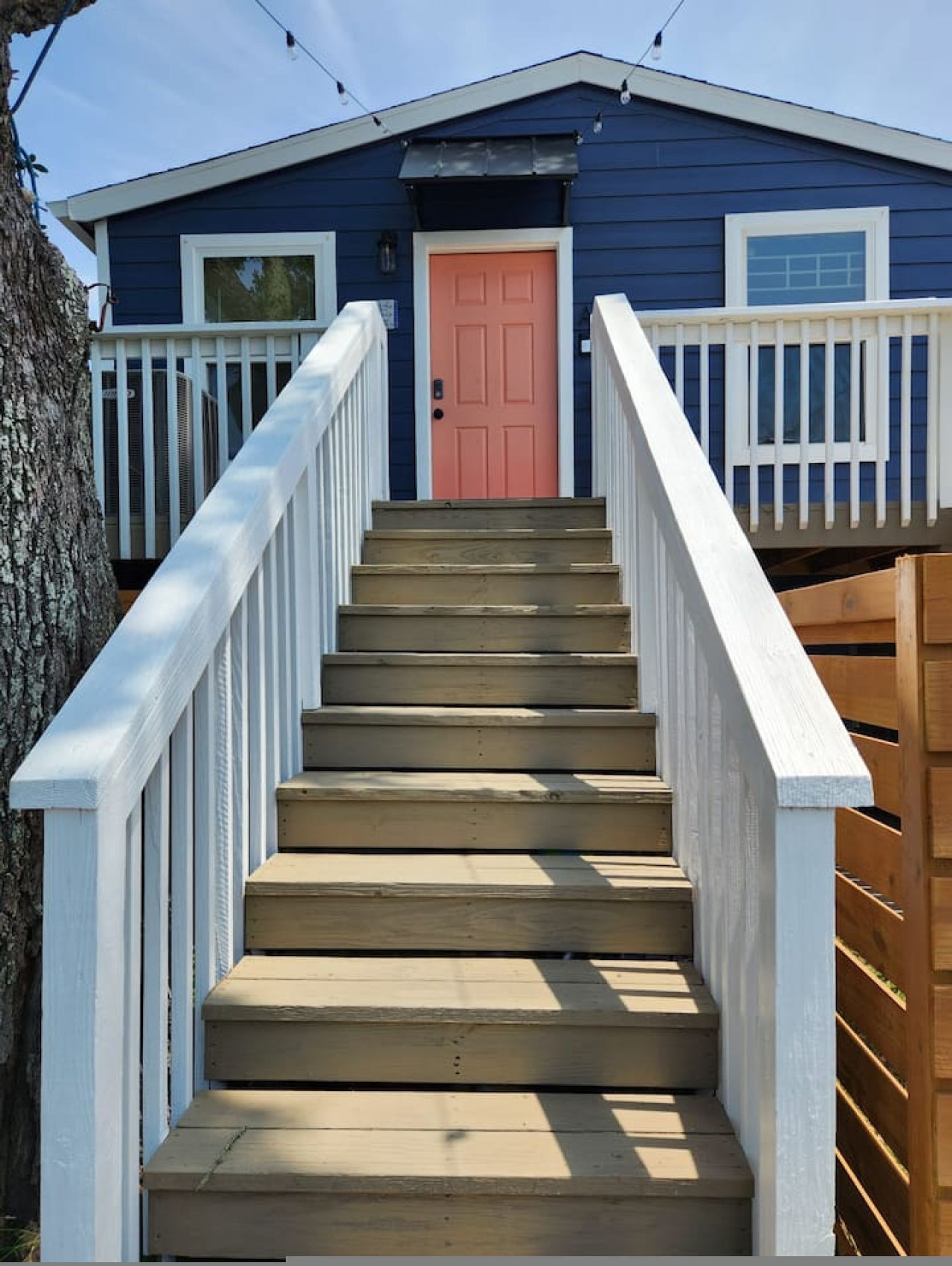 A wooden staircase leading to a blue house with a red door and white railings.