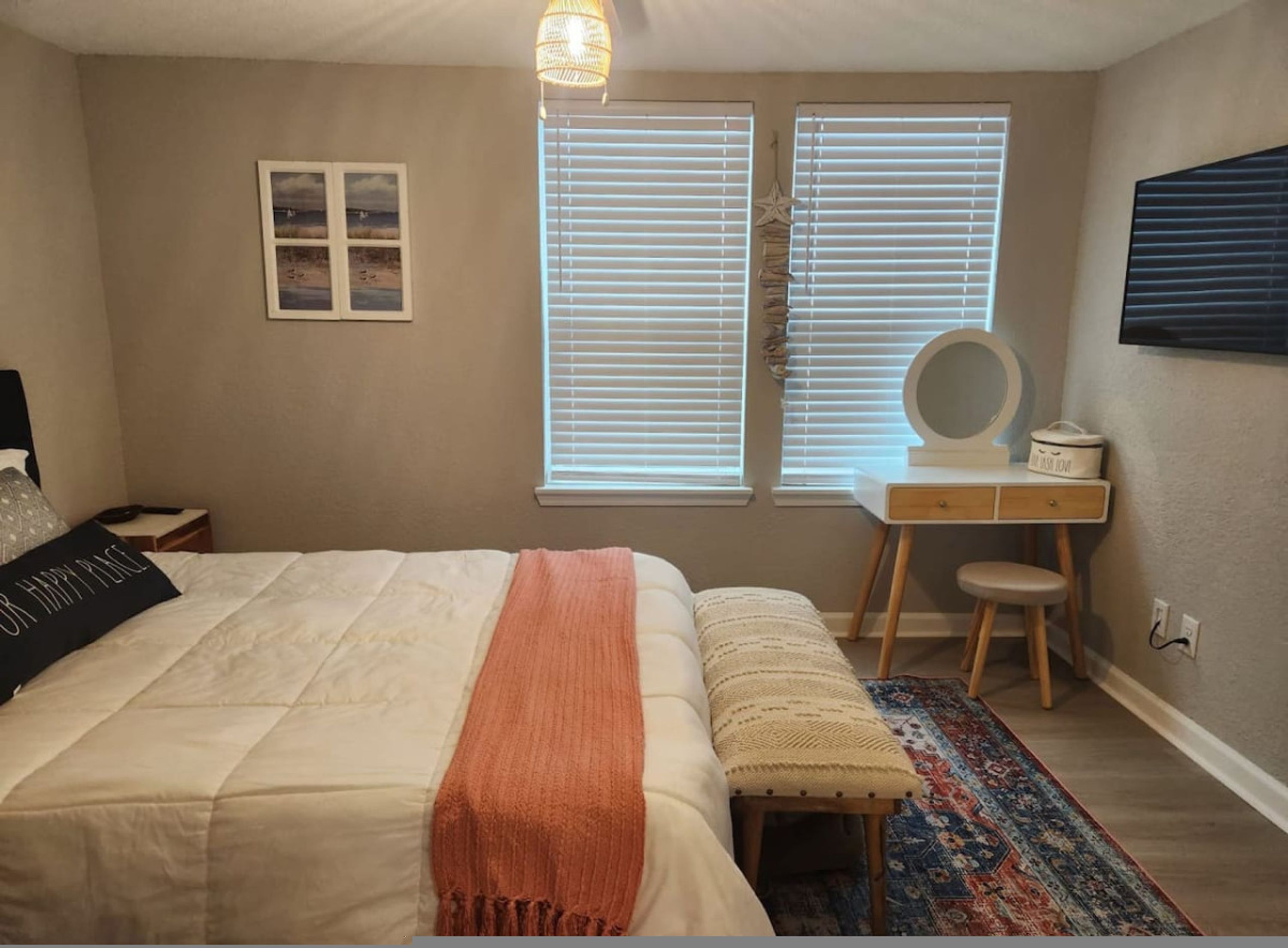A bedroom with a bed, a desk, a chair, a rug, and a wall-mounted mirror.