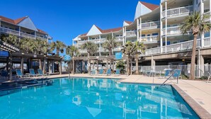 A swimming pool with lounge chairs and palm trees, surrounded by multi-story buildings with balconies.