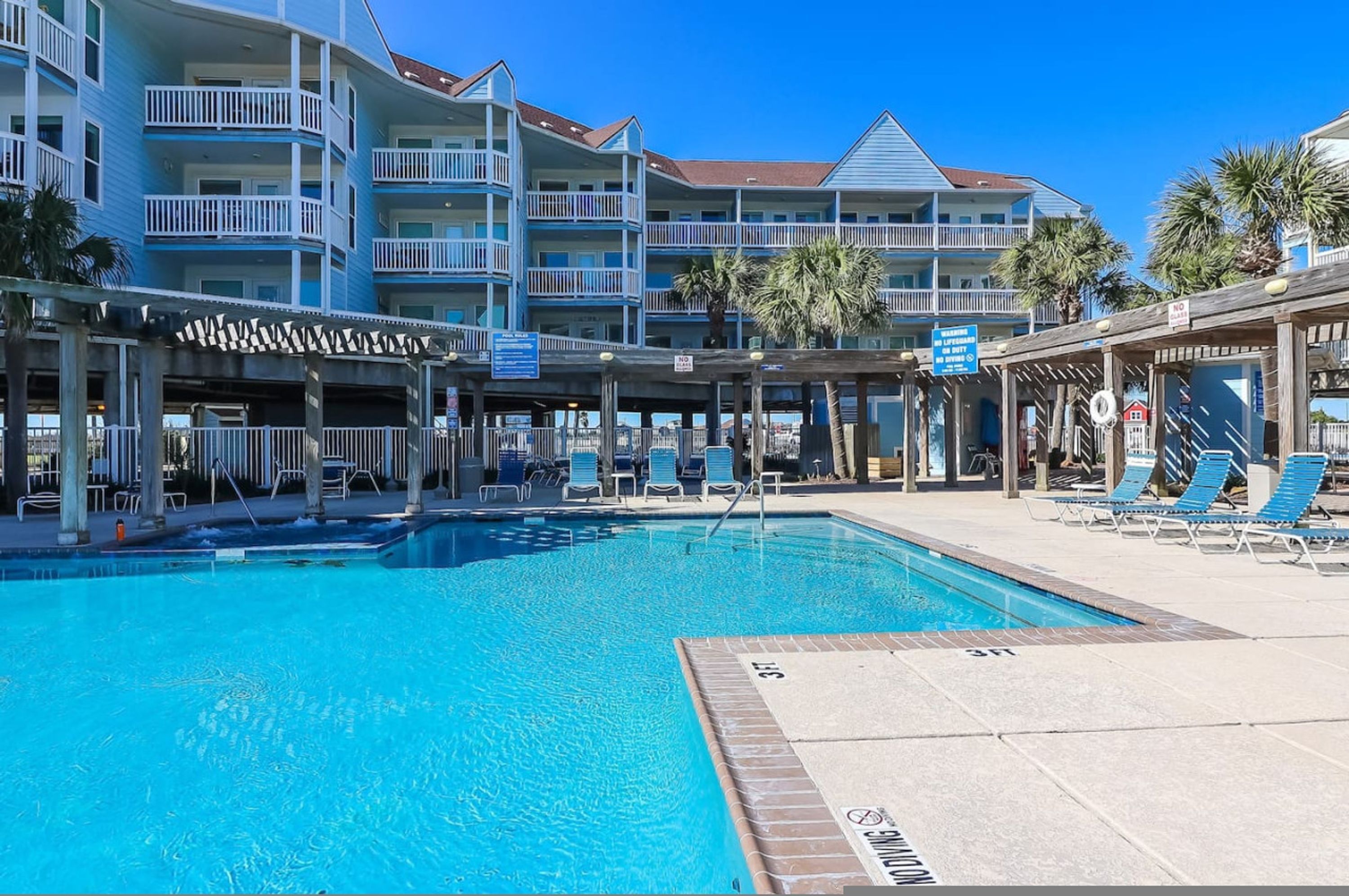 A swimming pool with lounge chairs and a covered area, surrounded by multi-story buildings with balconies.