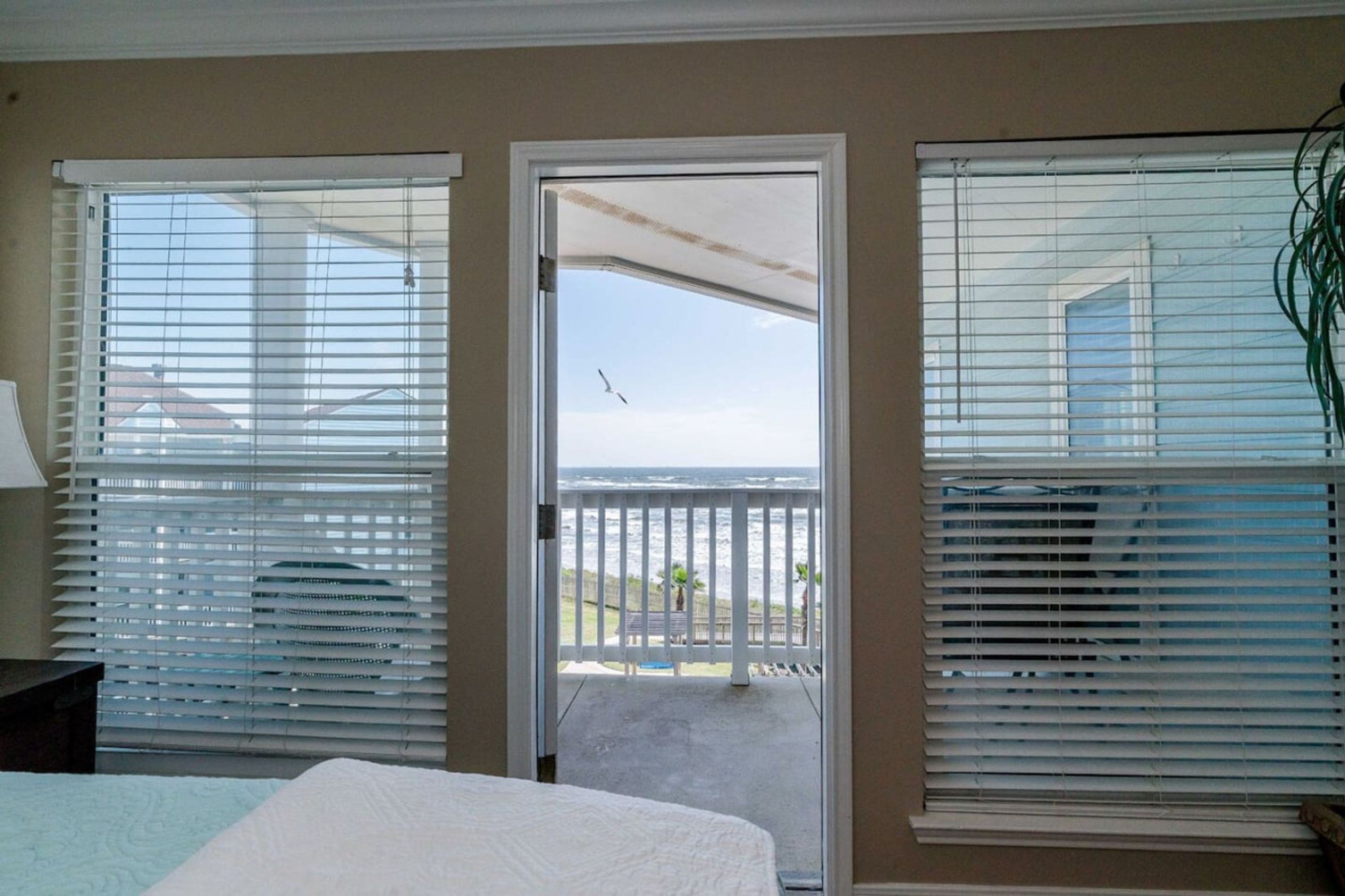 A hotel room with a bed, a nightstand, and a view of the ocean through a door.