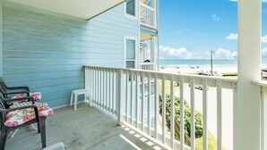Un balcon avec vue sur la plage, une petite table blanche et deux chaises dotées de coussins à motifs floraux.