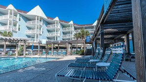 Un espace aménagé au bord de la piscine, avec des chaises longues, une piscine et un bâtiment doté de plusieurs balcons.