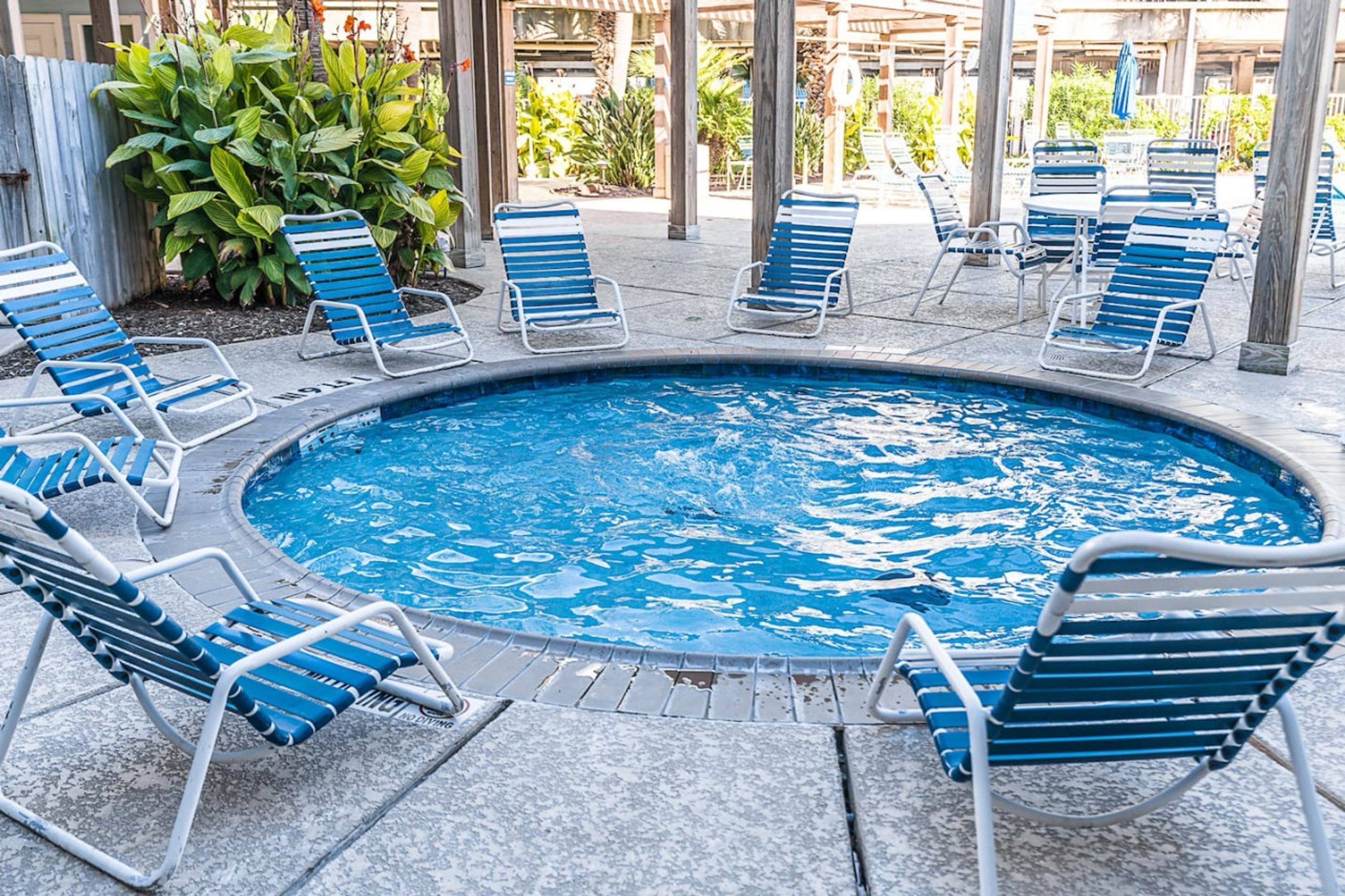 Uma área de piscina com cadeiras de descanso azuis e brancas dispostas ao redor de uma piscina circular.