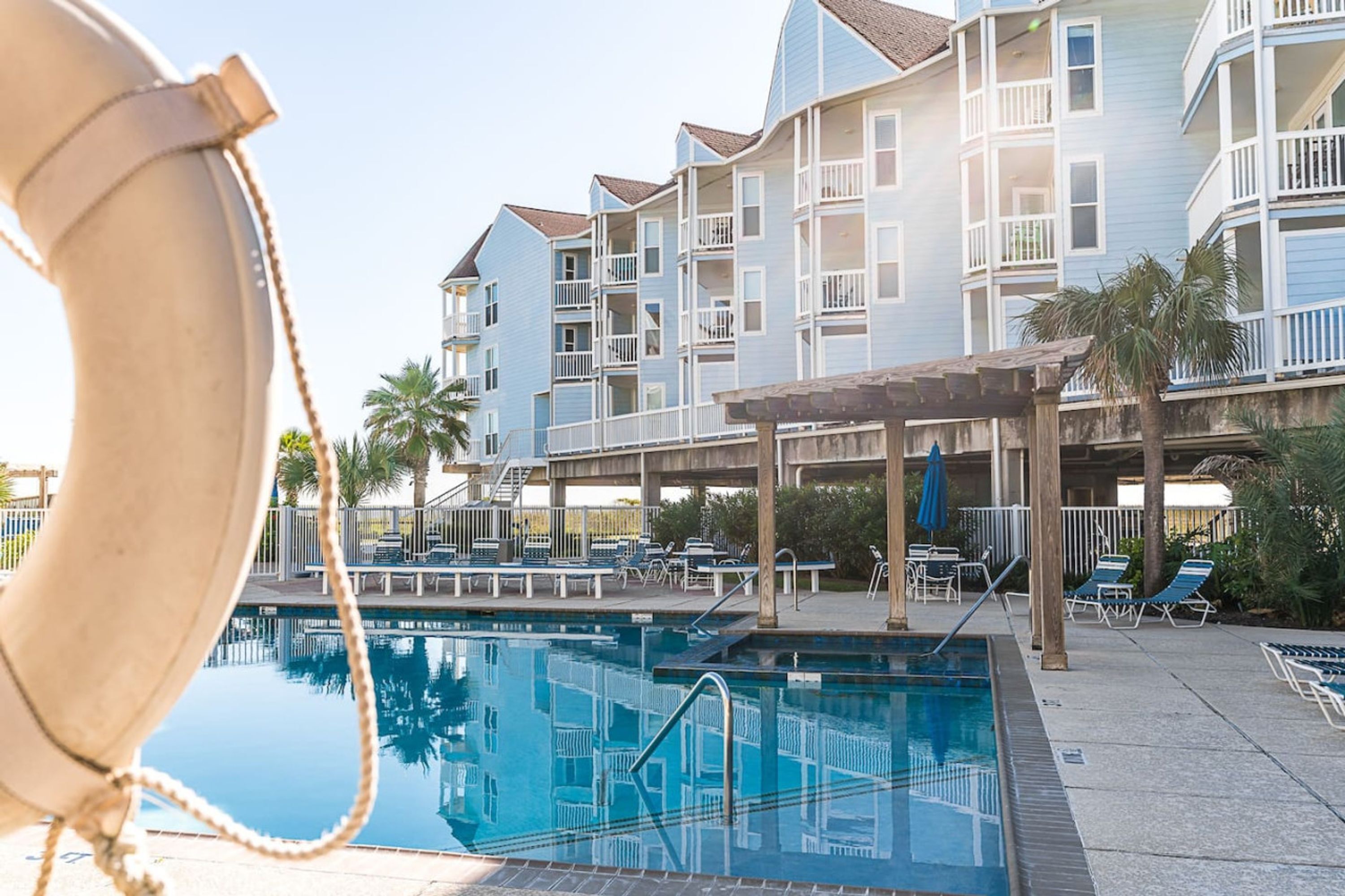 Une piscine avec des chaises longues et, au fond, un bâtiment doté de nombreux balcons.