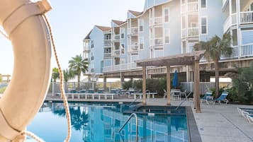 A swimming pool with lounge chairs and a building with multiple balconies in the background.