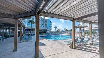A covered pool area with lounge chairs and a view of a multi-story building in the background.