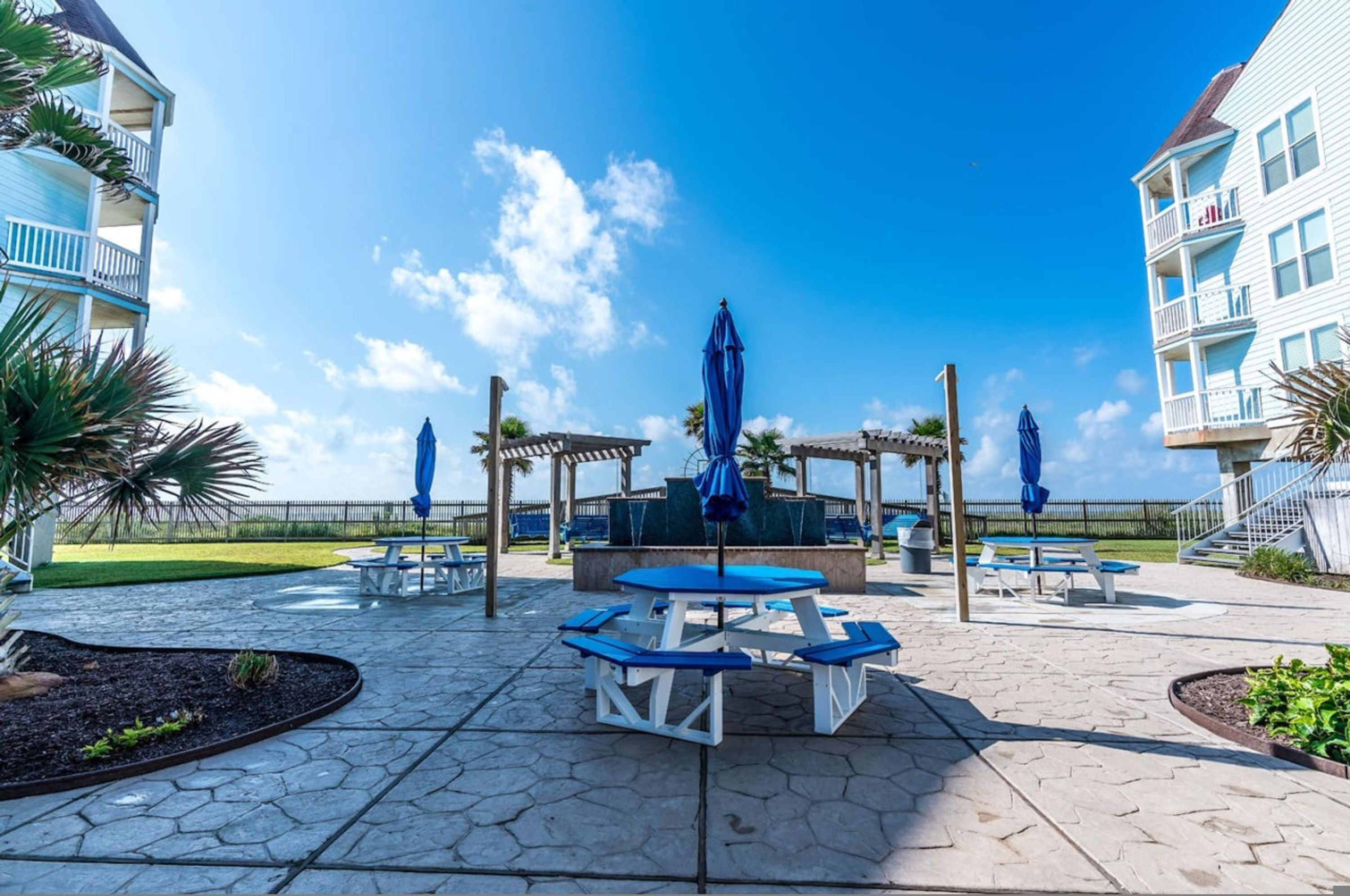 A patio area with picnic tables and umbrellas, surrounded by buildings with balconies.