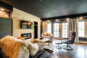 Ein modernes Wohnzimmer mit Kamin, einer Couch, einem Sessel und einem an der Wand befestigten Fernseher.