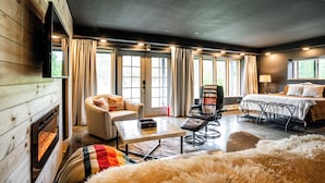 Una habitación acogedora con chimenea, un sofá, una silla, una cama y ventanas amplias.