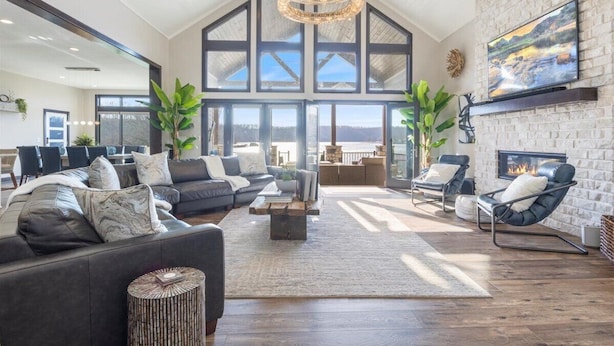 A spacious living room with a high ceiling, large windows, a fireplace, and a modern chandelier. - LOTO Pointe, Updated Luxury Home w/ Boat & PWC Slip, Boat Ramp, Firepits, Pool Table & More! (Versailles)