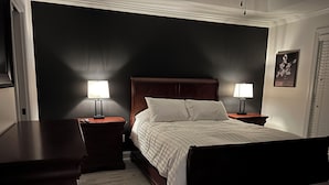 Une chambre à coucher bien rangée, avec un grand lit, deux tables de chevet avec des lampes et un tableau encadré au mur.