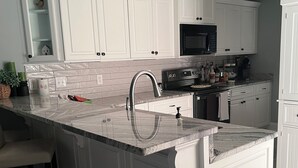 Une cuisine avec des meubles blancs, un plan de travail en granit et un évier en acier inoxydable.