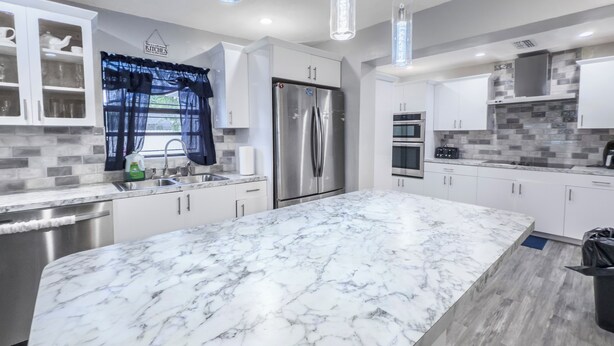 Een moderne keuken met een groot marmeren eiland, roestvrijstalen apparatuur en witte keukenkastjes.
