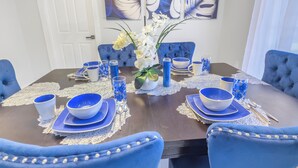Een eettafel gedekt met blauwe en witte borden, kommen en glazen, omringd door blauw beklede stoelen.