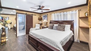 Ruime slaapkamer met een groot bed, een plafondventilator en uitzicht op de badkamer.
