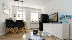 Et moderne køkken med et sort køleskab, et spiseområde med sorte stole og et glasbord med et magasin.