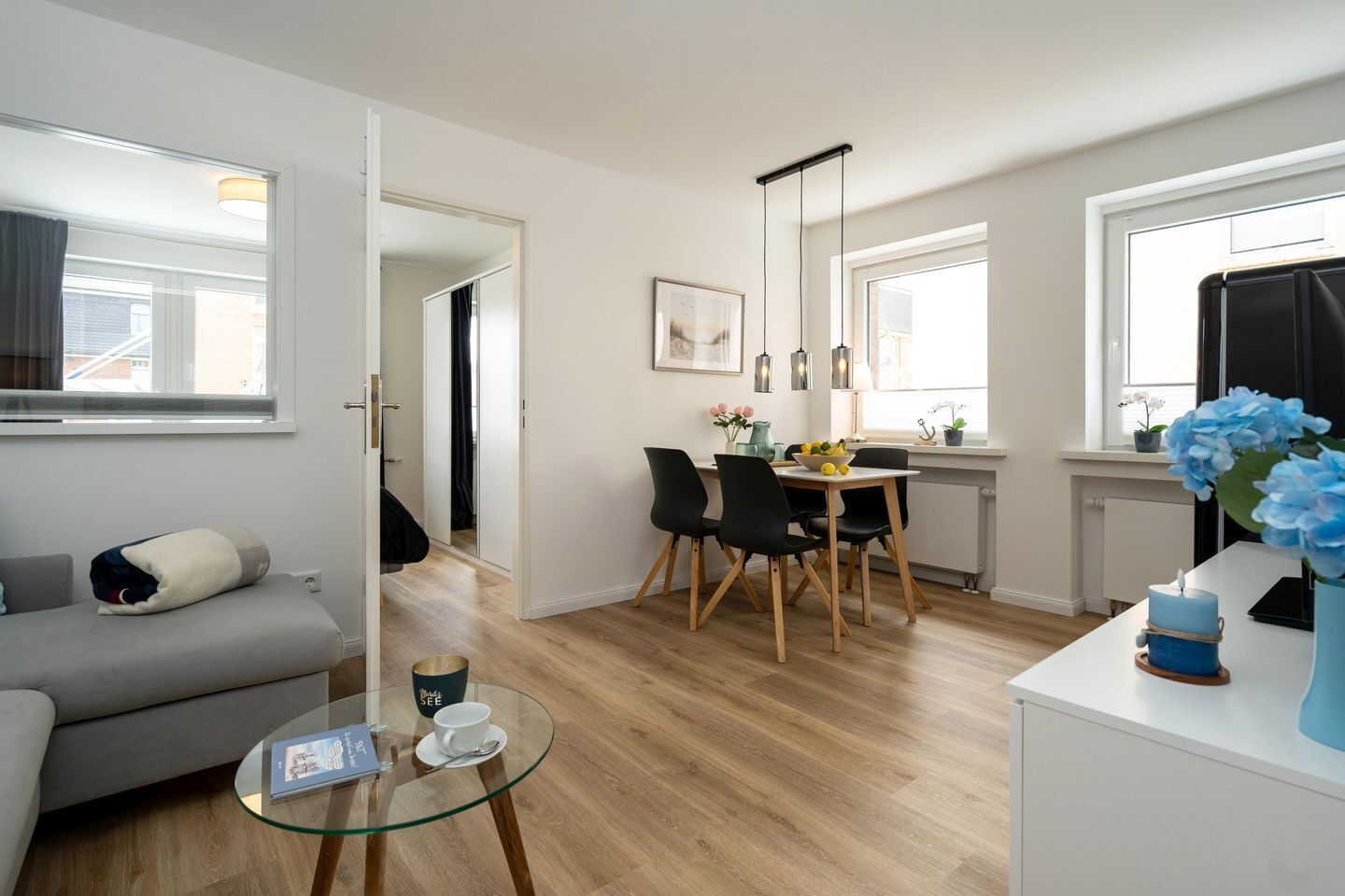 Eine moderne Wohnung mit Wohnzimmer, Essbereich und Küche. Es gibt ein Sofa, einen Glastisch und einen Esstisch mit Stühlen.
