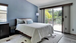 A bedroom with a large bed, a nightstand, a lamp, and a view of the outdoors through a sliding glass door. - Serene hillside oasis with pool, spa, & BBQ - 20 min to beach. 31-night minimum. (Oceanside)