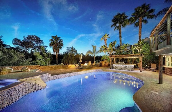Piscina con muelle de madera, palmeras y una pérgola con asientos.