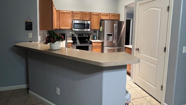 Una cocina moderna con una isla central, armarios de madera, electrodomésticos de acero inoxidable y suelo de baldosas.