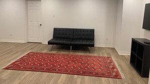 A room with a black sofa, a red patterned rug, a white door, and a TV on a black stand. - Spacious basement in nice area (Salaberry-de-Valleyfield)