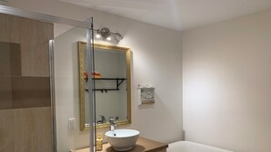 A bathroom with a glass shower enclosure, a white sink with a gold-framed mirror above it, and a white bathtub. - Spacious basement in nice area (Salaberry-de-Valleyfield)