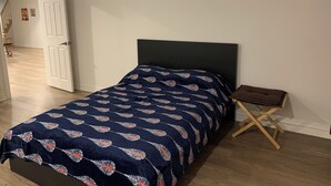 A bedroom with a bed, a small wooden nightstand, and a door leading to another room. - Spacious basement in nice area (Salaberry-de-Valleyfield)
