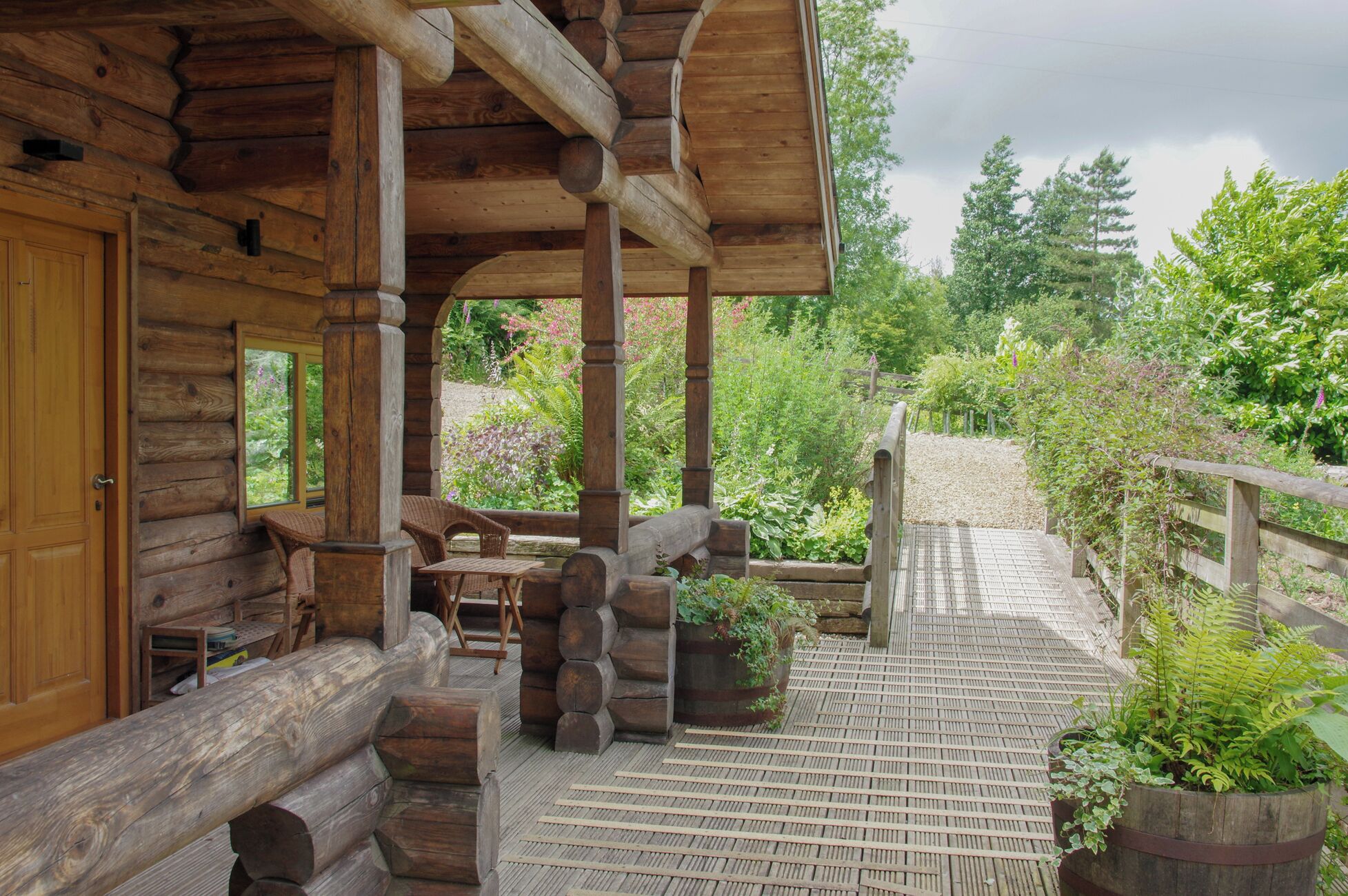 A log cabin with a wooden porch, outdoor seating, and a garden area.