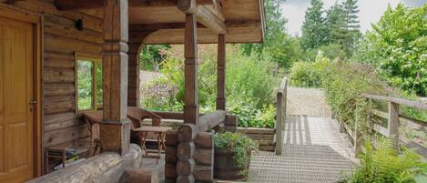 A log cabin with a wooden porch, outdoor seating, and a garden area.