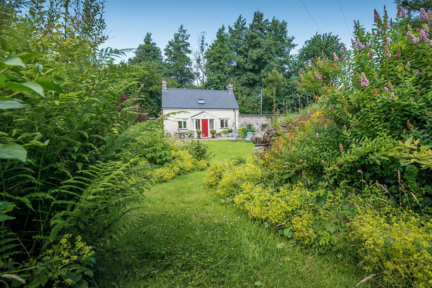 A stone house with a red door, surrounded by lush greenery and a well-maintained garden.