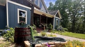 Ein Haus mit einer Steinterrasse, einem kleinen Teich und einer bunten Blumenpracht im Garten.