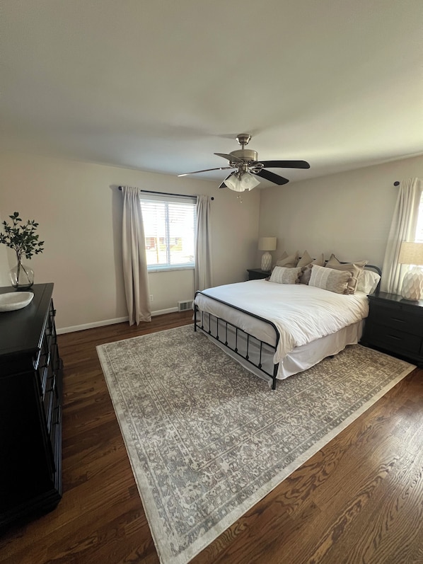 A bedroom with a bed, a ceiling fan, a nightstand, a dresser, and a window with curtains. - Charming 2-Bedroom Apartment in Cincinnati (Cincinnati)