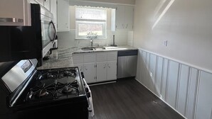 Une cuisine équipée d’une cuisinière, d’un évier et d’un lave-vaisselle, avec des meubles blancs et une fenêtre.