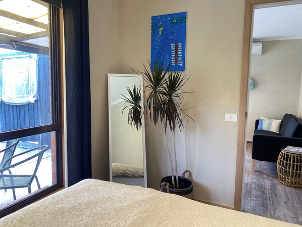 Hotelkamer met een bed, een potplant, een spiegel, een blauw kunstwerk en uitzicht op buiten.