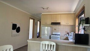 A compact kitchen with wooden cabinets, a white refrigerator, a stove, and a small dining area with a white chair.