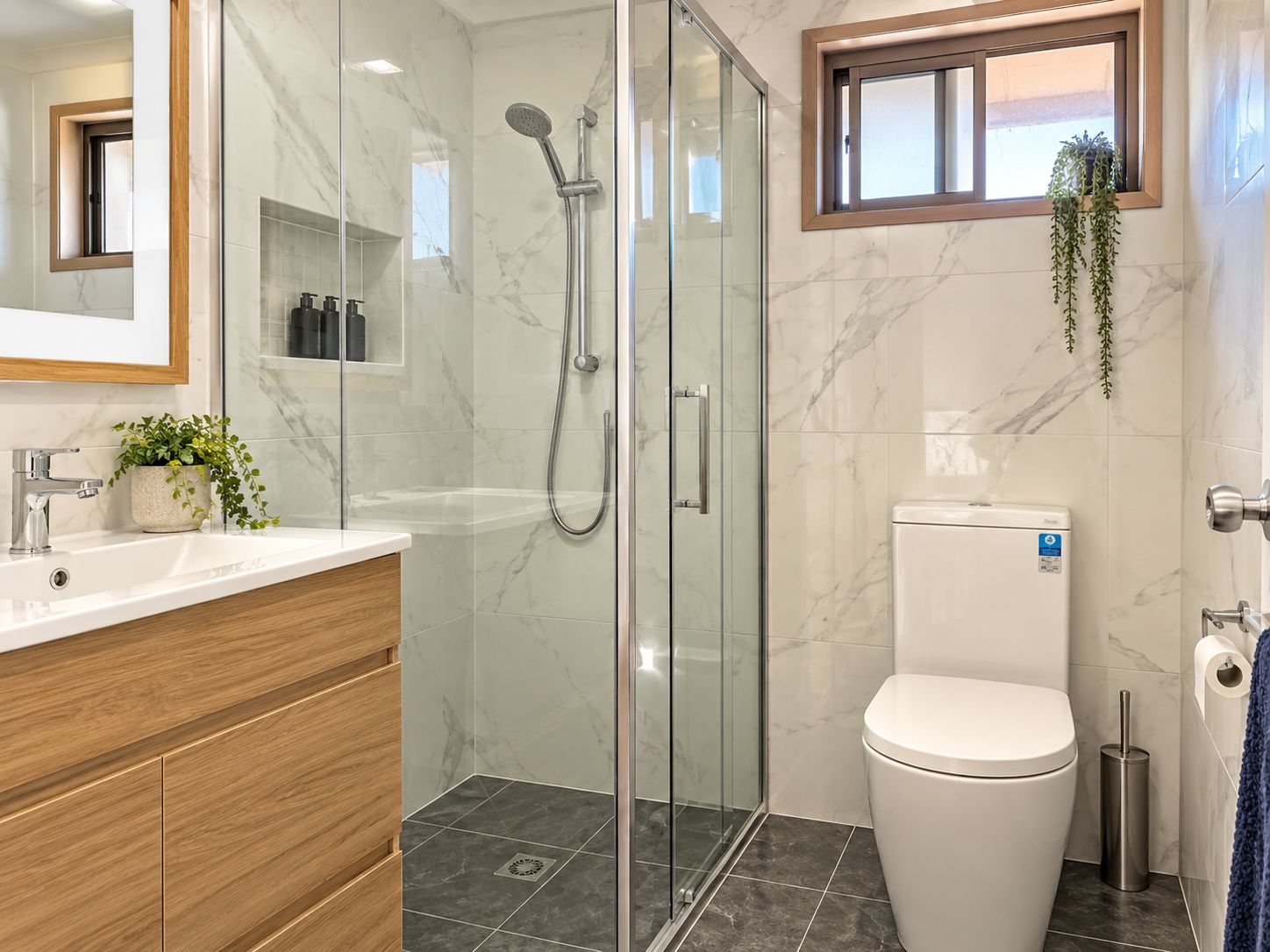 A modern bathroom with a glass-enclosed shower, a white toilet, and a wooden vanity.