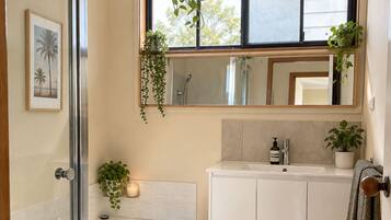 A modern bathroom with a glass shower enclosure, a freestanding bathtub, a vanity with a mirror, and potted plants.