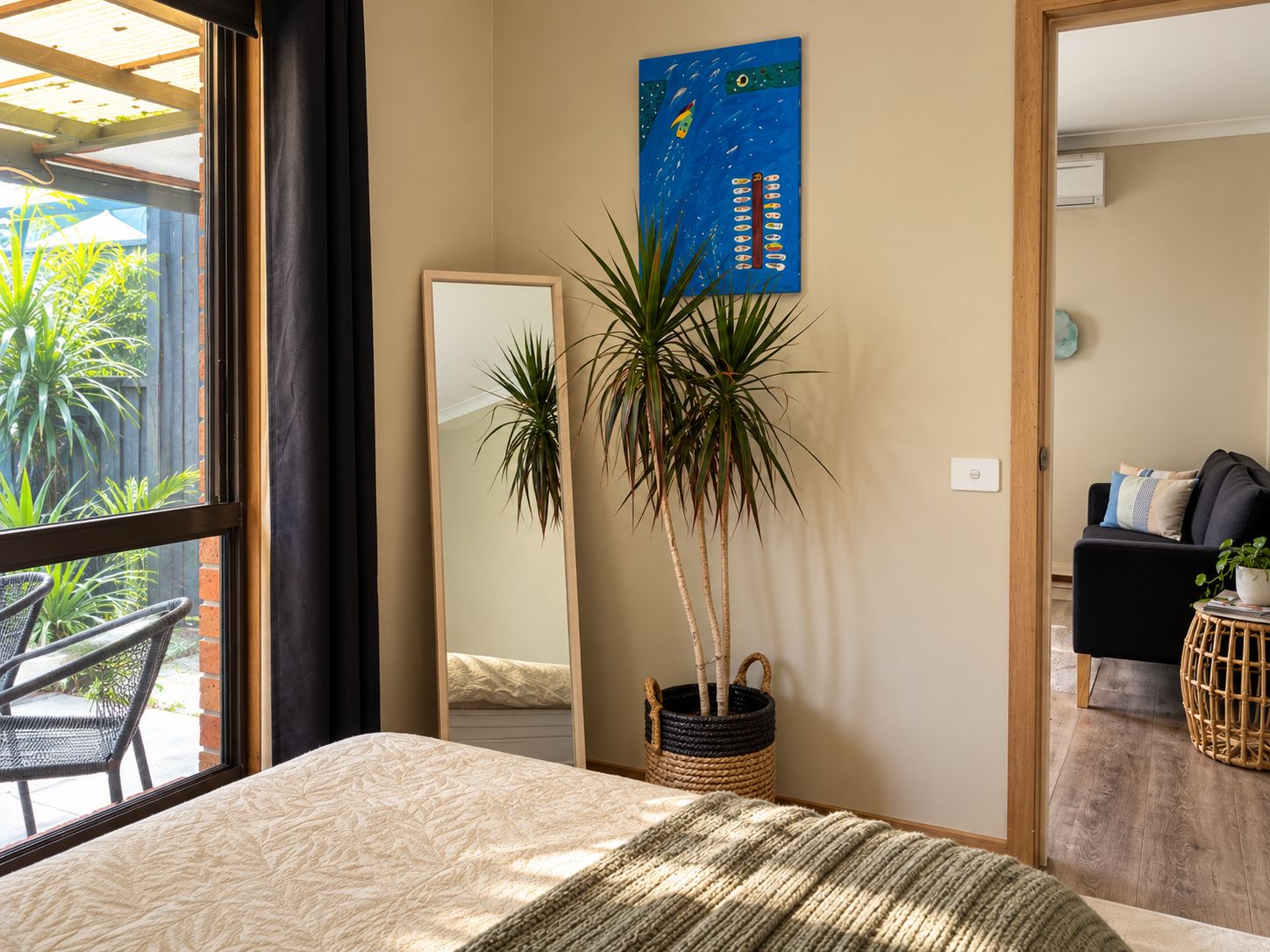Una camera da letto con un letto, uno specchio grande, una pianta in vaso e vista sull'esterno.