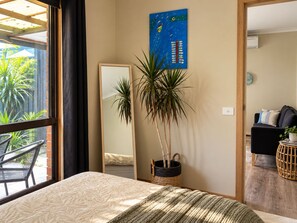 A bedroom with a bed, a large mirror, a potted plant, and a view of the outdoors. - Beachside Retreat - Rosebud (Rosebud)