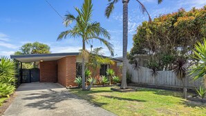 A residential property with a brick house, a paved driveway, and a fenced yard with various plants and trees.