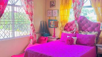 A bedroom with a large bed, curtains, a nightstand, a lamp, and a window with a view of greenery.