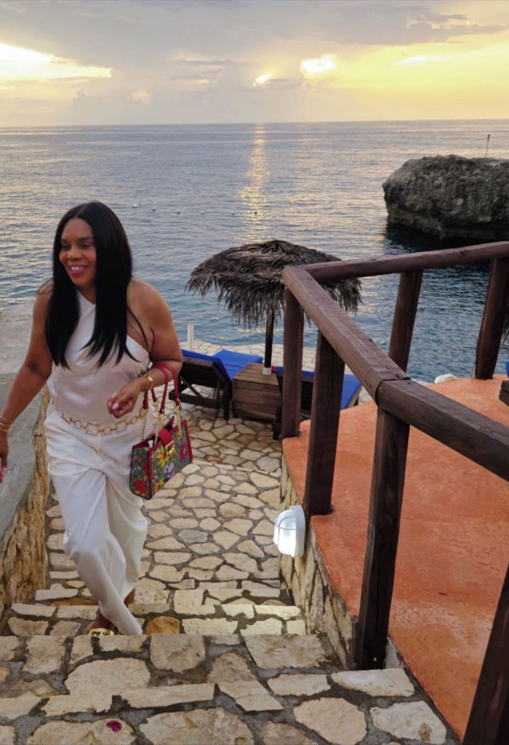 A person descending a stone staircase with a view of the sea and a thatched structure in the background.